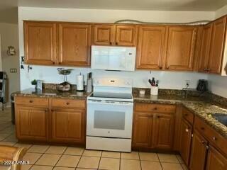 kitchen with light tile patterned floors, dark stone counters, and white appliances