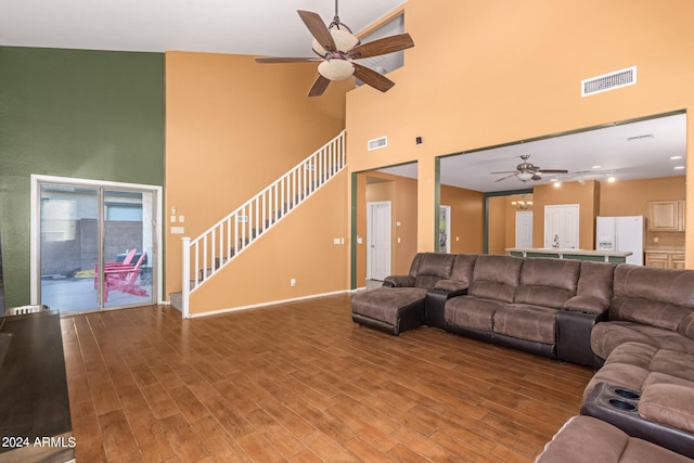 living room with a towering ceiling, hardwood / wood-style floors, and ceiling fan