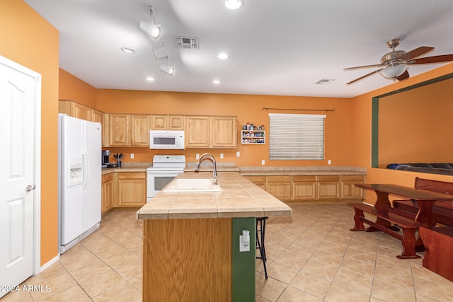 kitchen with white appliances, light brown cabinetry, sink, a kitchen bar, and a kitchen island with sink