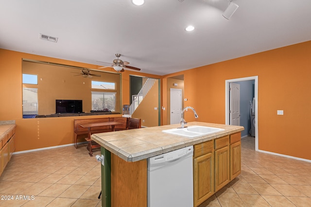 kitchen with dishwasher, tile countertops, an island with sink, sink, and light tile patterned floors