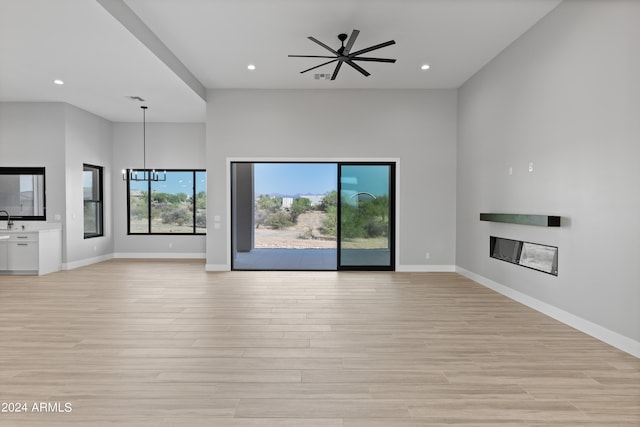 unfurnished living room featuring light hardwood / wood-style flooring, sink, and ceiling fan with notable chandelier