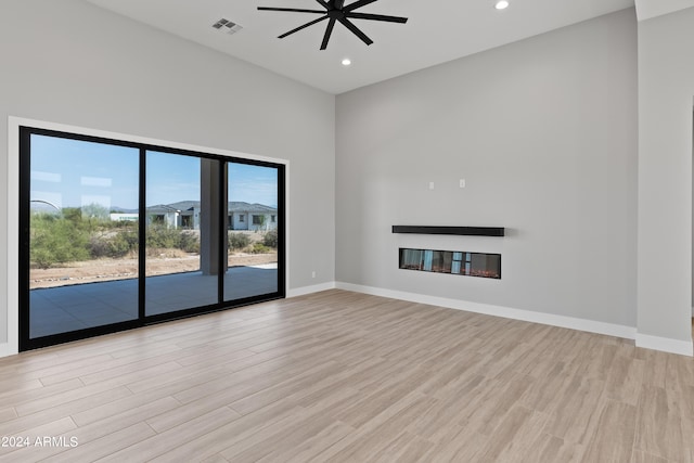 unfurnished living room with light hardwood / wood-style floors, a towering ceiling, and ceiling fan