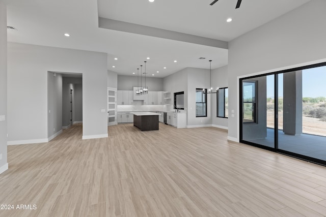 unfurnished living room featuring ceiling fan with notable chandelier and light wood-type flooring