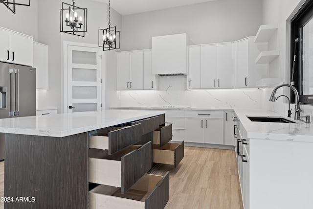 kitchen featuring white cabinets, high end refrigerator, a kitchen island, a high ceiling, and sink