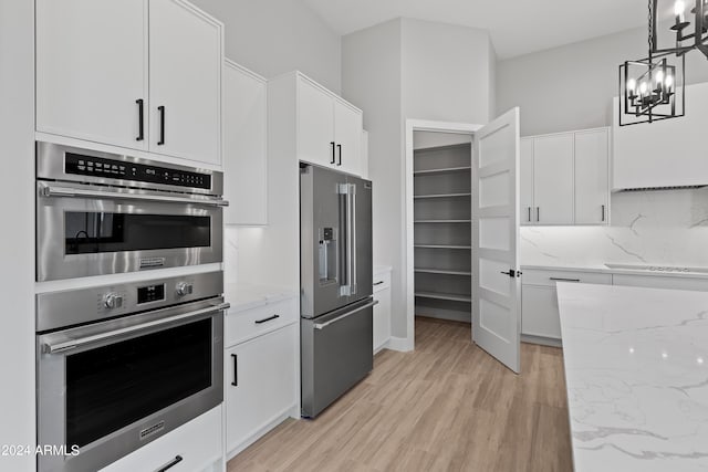 kitchen with white cabinets, hanging light fixtures, backsplash, light wood-type flooring, and stainless steel appliances