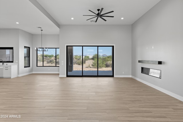 unfurnished living room featuring sink, a high ceiling, light wood-type flooring, and ceiling fan with notable chandelier