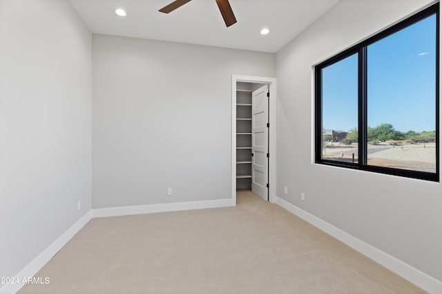 unfurnished bedroom featuring a walk in closet, light colored carpet, and ceiling fan