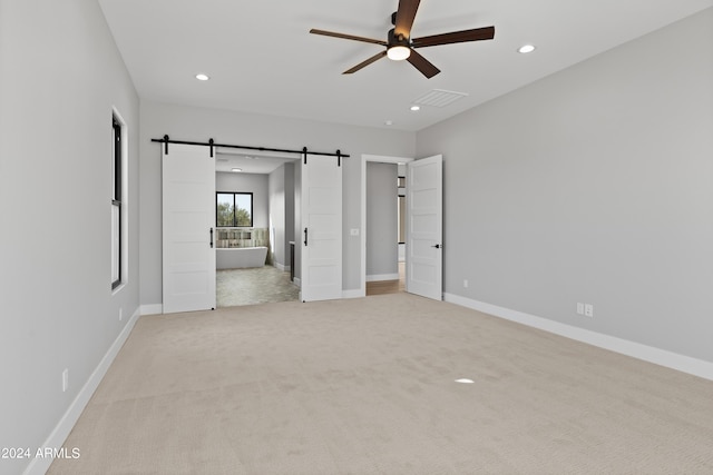 unfurnished bedroom featuring connected bathroom, a barn door, light carpet, and ceiling fan