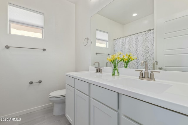 bathroom featuring a sink, baseboards, toilet, and a healthy amount of sunlight