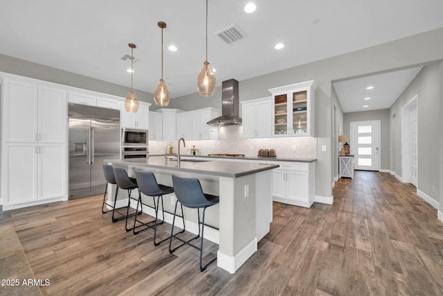 17565 E Blaze Ln, Rio Verde, AZ 85263 - kitchen featuring wall chimney range hood, built in appliances, backsplash, light wood-type flooring, and a breakfast bar area