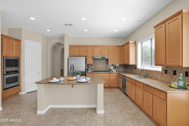 kitchen featuring sink, a kitchen island, light stone counters, stainless steel appliances, and extractor fan