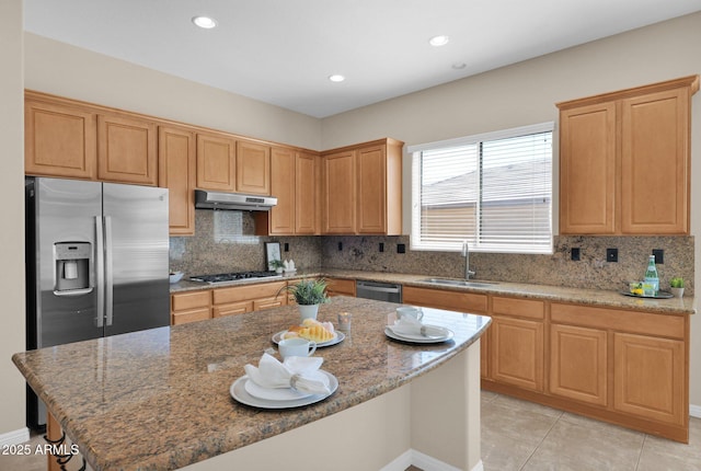 kitchen with light stone counters, stainless steel appliances, sink, light tile patterned floors, and a kitchen island