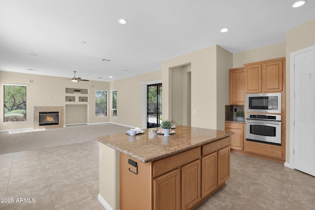 kitchen featuring a center island, ceiling fan, light tile patterned floors, light stone countertops, and appliances with stainless steel finishes