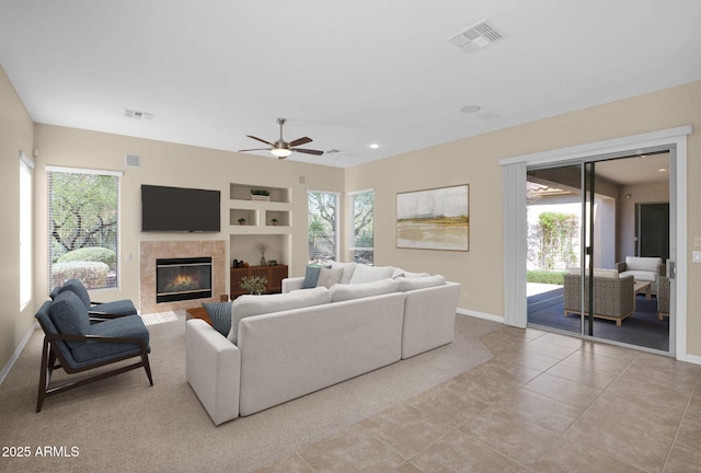 tiled living room with a tile fireplace, built in features, and ceiling fan