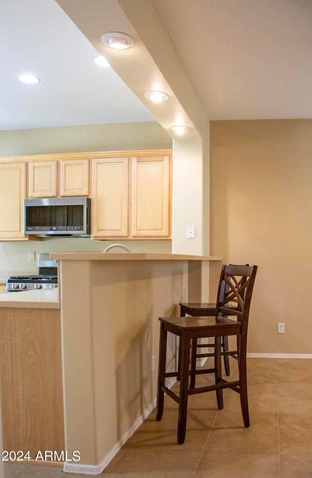 kitchen featuring a breakfast bar, kitchen peninsula, stainless steel appliances, light brown cabinets, and light tile patterned floors