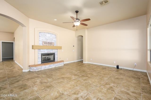 unfurnished living room featuring ceiling fan and a stone fireplace