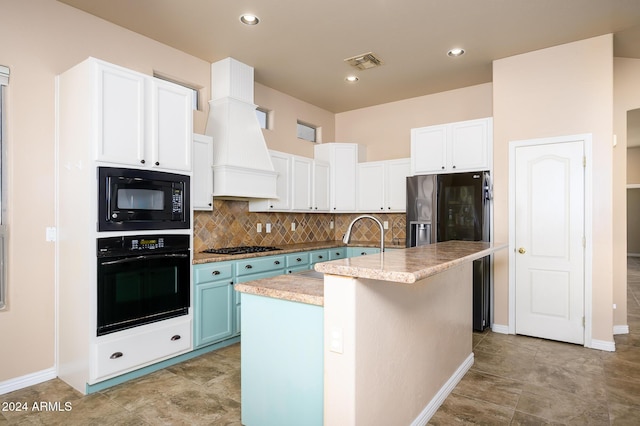 kitchen with decorative backsplash, custom range hood, black appliances, a center island with sink, and white cabinets