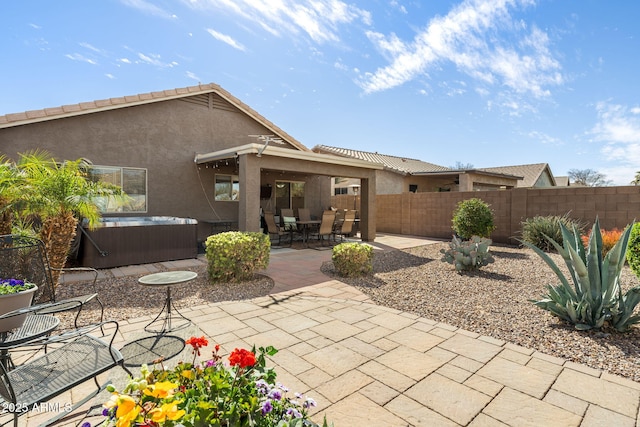 rear view of house featuring stucco siding, a patio area, a fenced backyard, and a hot tub