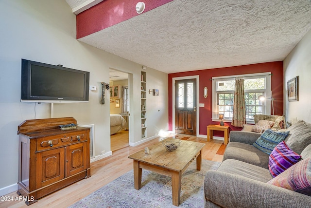 living room with light wood finished floors, a textured ceiling, baseboards, and built in shelves