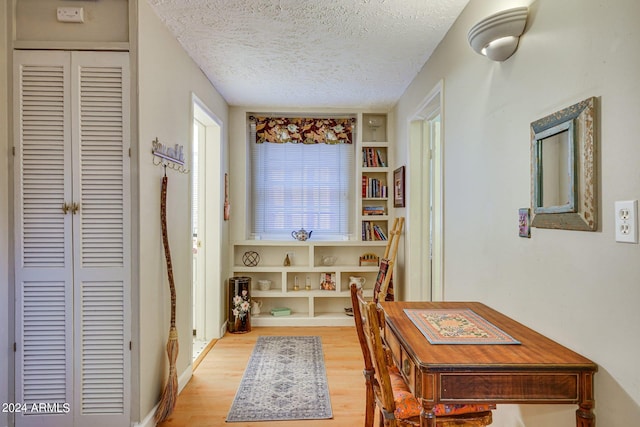 corridor with a textured ceiling, built in features, baseboards, and light wood-type flooring