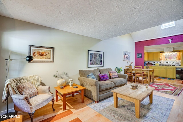 living room featuring vaulted ceiling, a textured ceiling, and light wood-style flooring