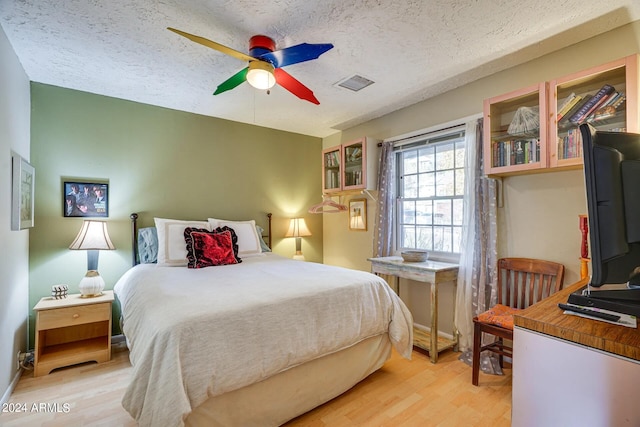 bedroom featuring light wood-style floors, visible vents, a ceiling fan, and a textured ceiling