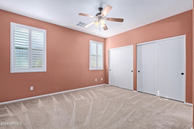 unfurnished bedroom featuring multiple windows, two closets, light colored carpet, and ceiling fan