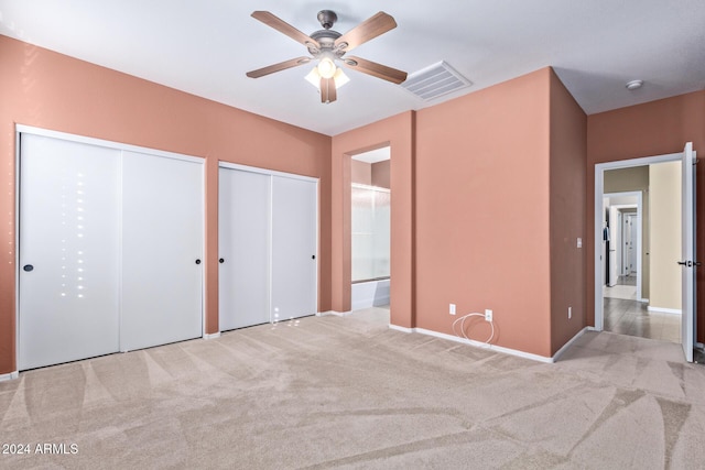 unfurnished bedroom with multiple closets, light colored carpet, ceiling fan, and ensuite bathroom