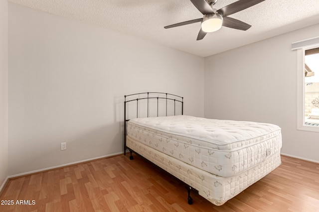 bedroom featuring a textured ceiling, multiple windows, baseboards, and wood finished floors