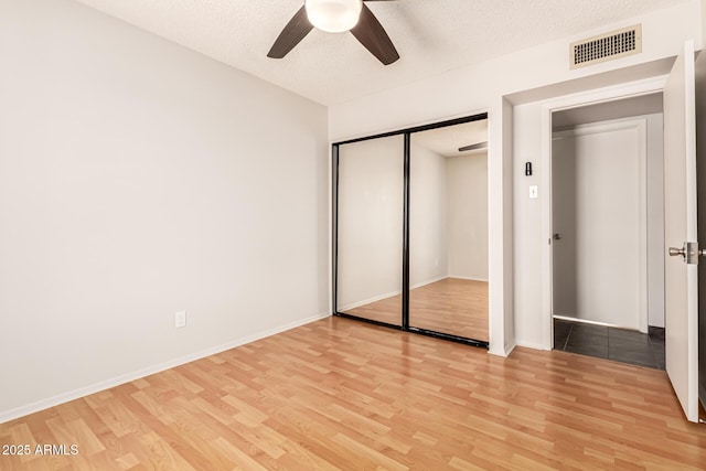 unfurnished bedroom featuring a ceiling fan, a textured ceiling, visible vents, a closet, and light wood finished floors