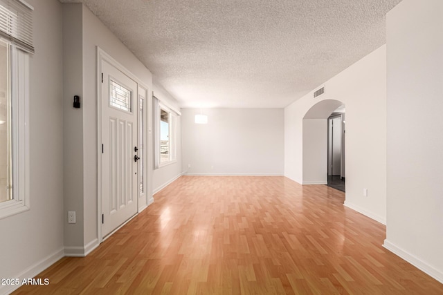 entrance foyer with arched walkways, a textured ceiling, visible vents, and light wood finished floors