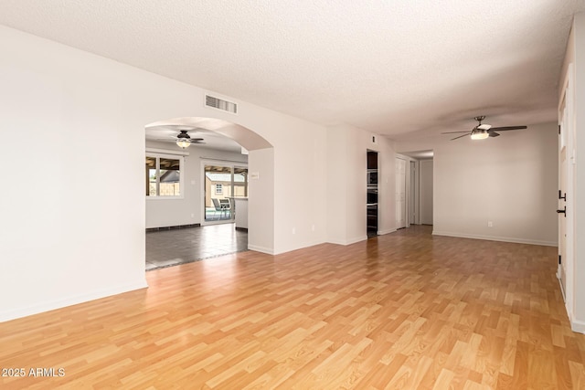 spare room featuring light wood-type flooring, a ceiling fan, arched walkways, and visible vents