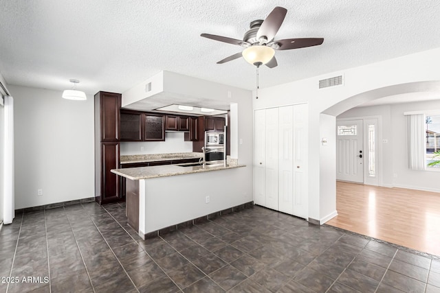 kitchen with dark brown cabinetry, arched walkways, a peninsula, stainless steel appliances, and visible vents