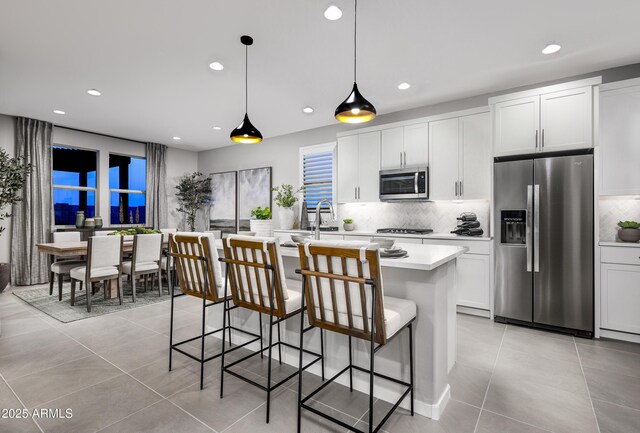 kitchen with appliances with stainless steel finishes, white cabinetry, a kitchen breakfast bar, hanging light fixtures, and a kitchen island with sink