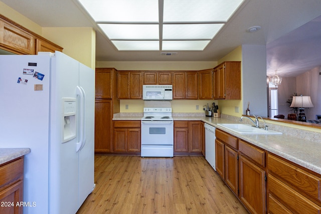 kitchen with sink, white appliances, light hardwood / wood-style floors, kitchen peninsula, and an inviting chandelier