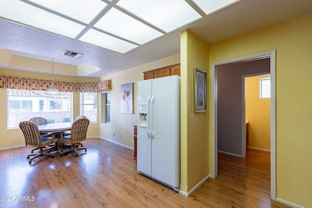 kitchen featuring a tray ceiling, white refrigerator with ice dispenser, light hardwood / wood-style floors, and hanging light fixtures