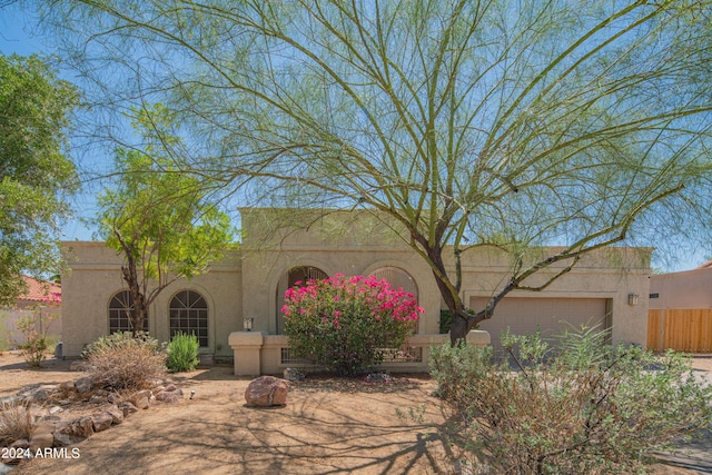 pueblo-style house with fence, an attached garage, and stucco siding