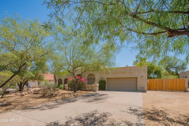 pueblo-style home featuring a garage, driveway, fence, and stucco siding