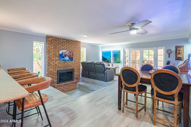 dining space with ornamental molding, light hardwood / wood-style flooring, a brick fireplace, ceiling fan, and french doors