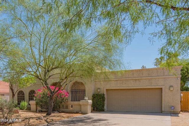 pueblo-style home featuring driveway, fence, an attached garage, and stucco siding