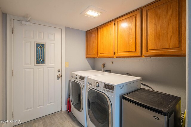 laundry area with washing machine and clothes dryer, cabinets, and light hardwood / wood-style floors