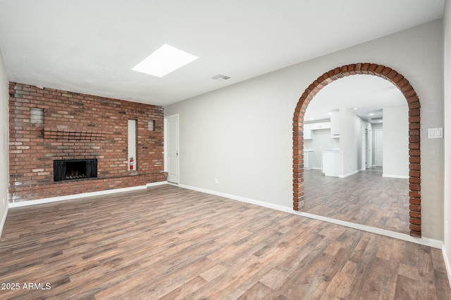 6223 W Earll Dr, Phoenix, AZ 85033 - unfurnished living room with a skylight, wood finished floors, a fireplace, and arched walkways