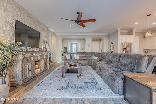 living room with crown molding, light hardwood / wood-style flooring, a stone fireplace, and ceiling fan