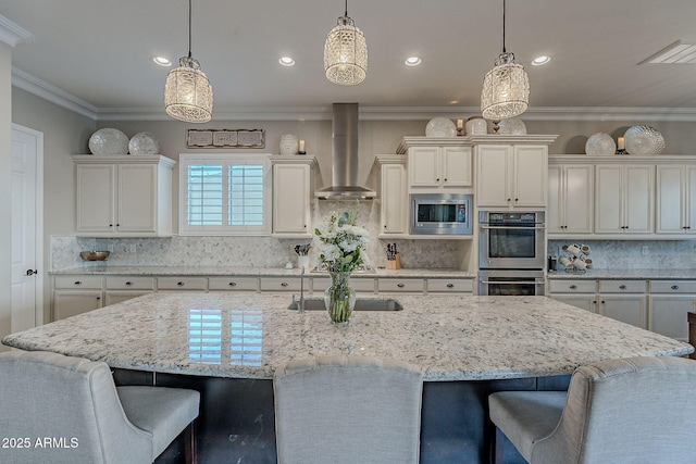 kitchen with pendant lighting, backsplash, stainless steel appliances, wall chimney exhaust hood, and a large island with sink