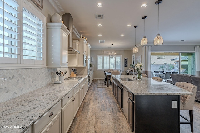 kitchen with sink, a kitchen island with sink, light stone counters, tasteful backsplash, and decorative light fixtures