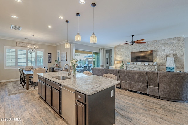 kitchen with pendant lighting, sink, a kitchen island with sink, light stone counters, and ornamental molding