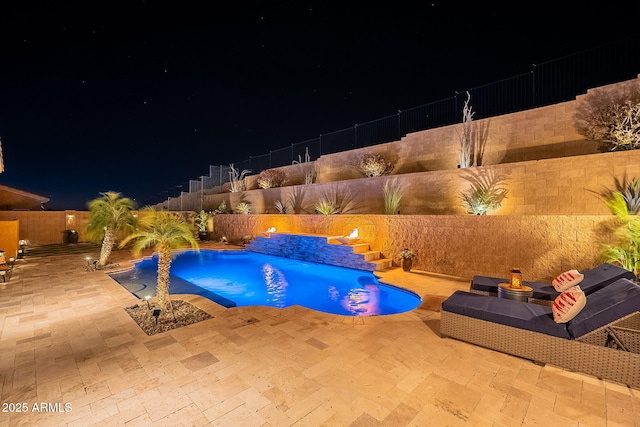 pool at night featuring pool water feature and a patio area