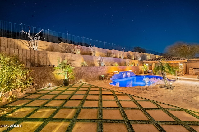 pool at night with pool water feature and a patio area