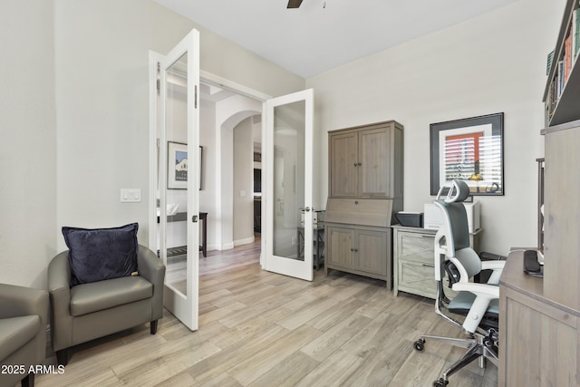 office with light wood-style floors, arched walkways, a ceiling fan, and french doors