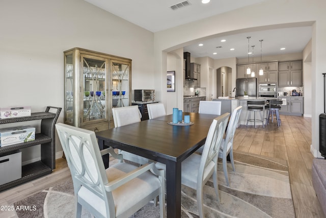 dining room with light wood-type flooring, arched walkways, visible vents, and recessed lighting